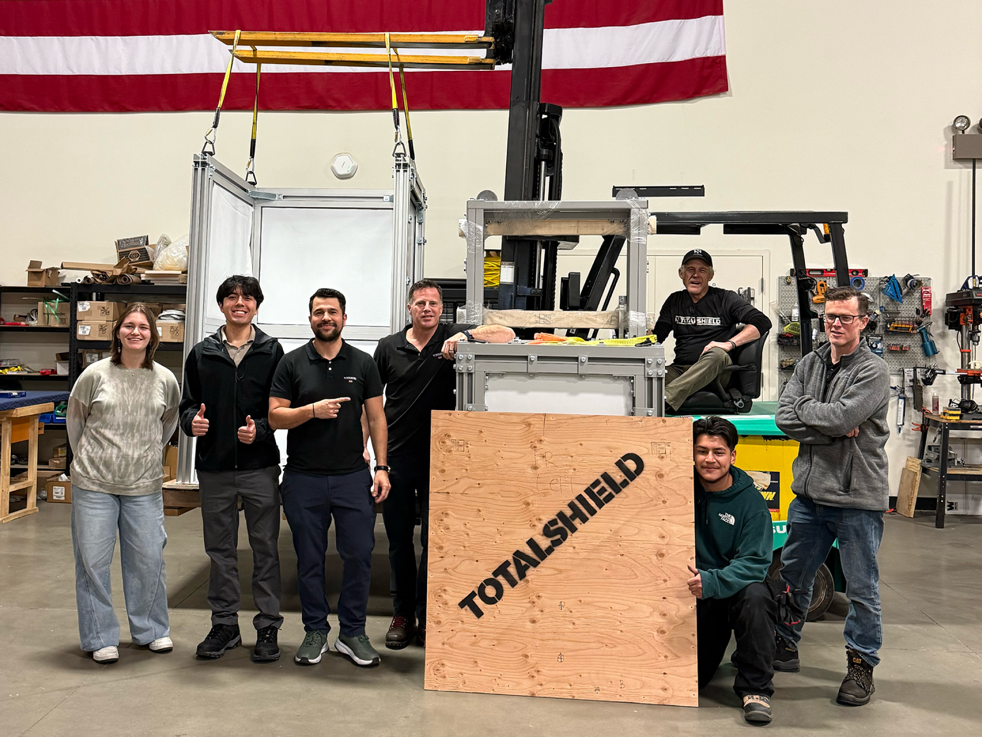 Photo of the TotalShield team smiling next to an enclosure and a crate.